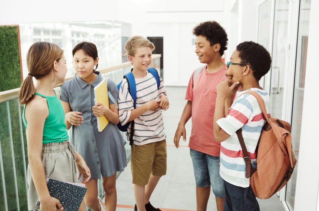 pexels-photo-8456153-8456153 Diverse group of students talking and laughing in a school hallway, holding books and bags.