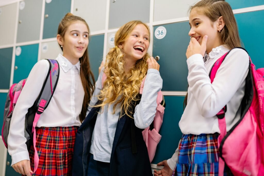 pexels-photo-8617647-8617647 Three girls in school uniforms laughing and talking by lockers, indoors.